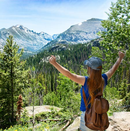 Woman with raised hands relaxing on top of the mountain, looking at beautiful summer landscape. View of Long Peak, Rocky Mountains National Park, Colorado, USA.