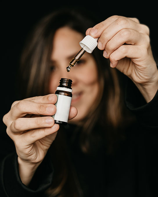 Woman holding a dropper pipette sublingual Cannabis oil at black background