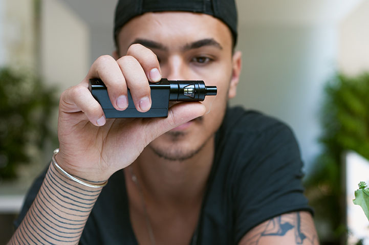 young bearded man holds a vape pen