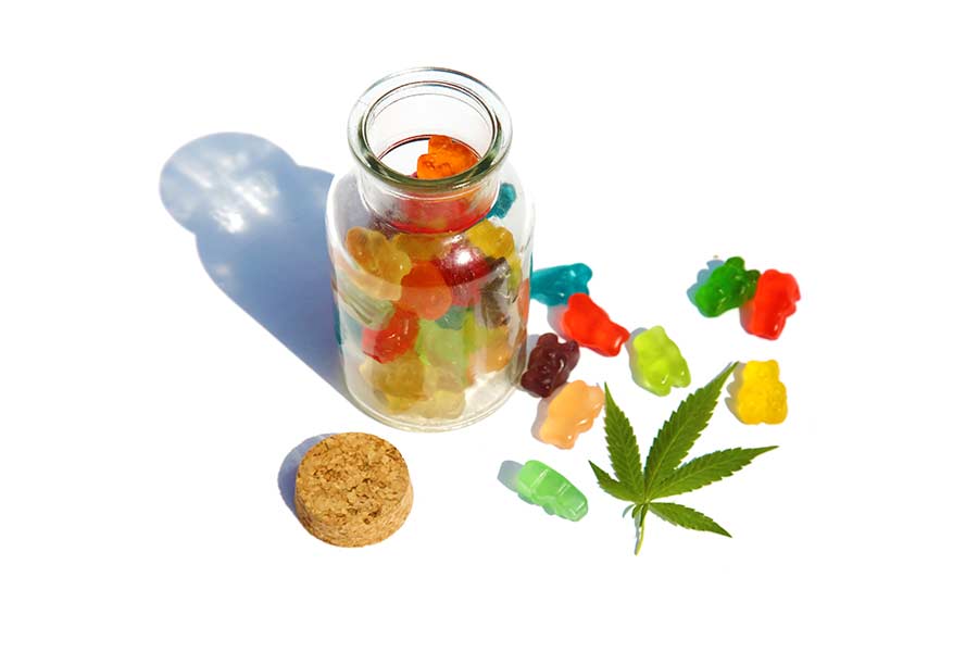 a jar full of cannabis gummy bears next to a pot leaf
