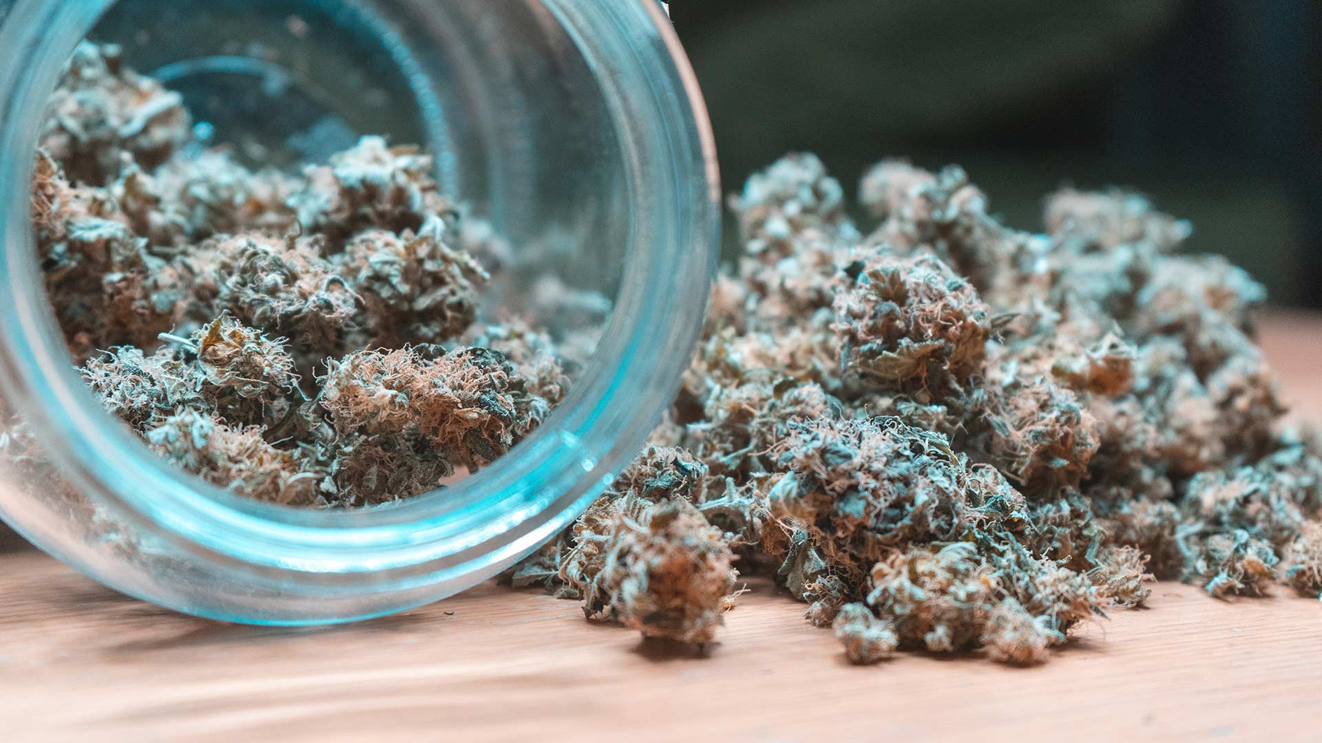 cannabis flower spilling out a glass jar on it's side