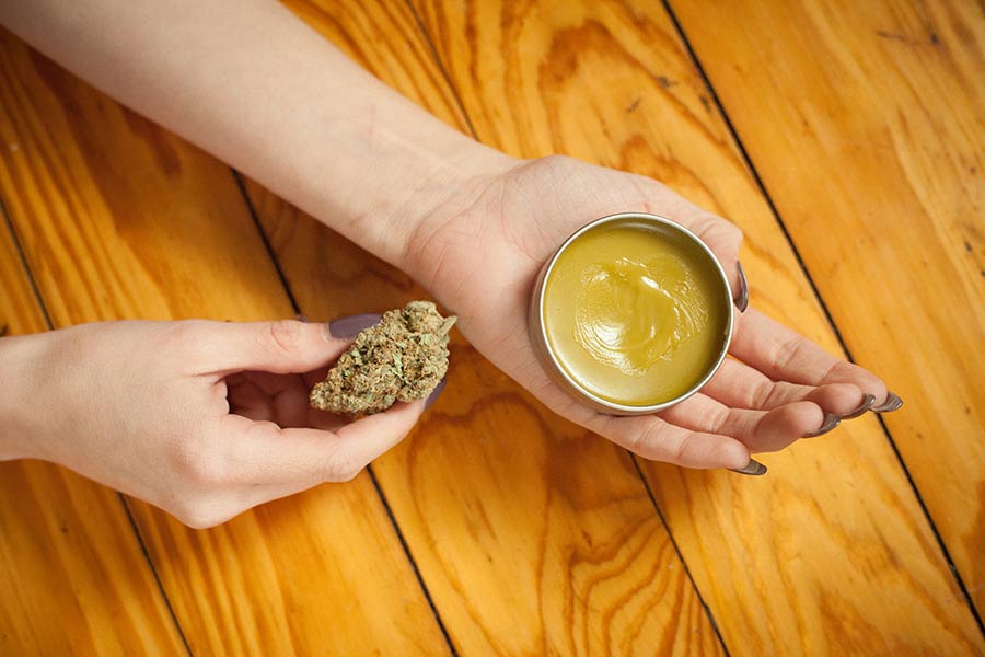 woman holding cannabis balm in left hand and cannabis flower in right hand